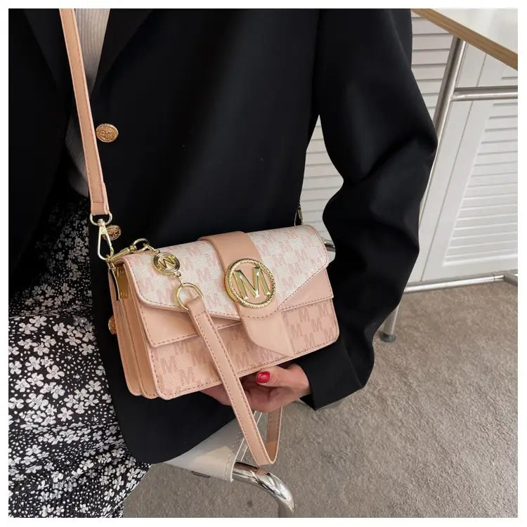 A blush pink monogram letter print crossbody messenger bag with gold-tone hardware and an elegant flap closure featuring a circular logo emblem.