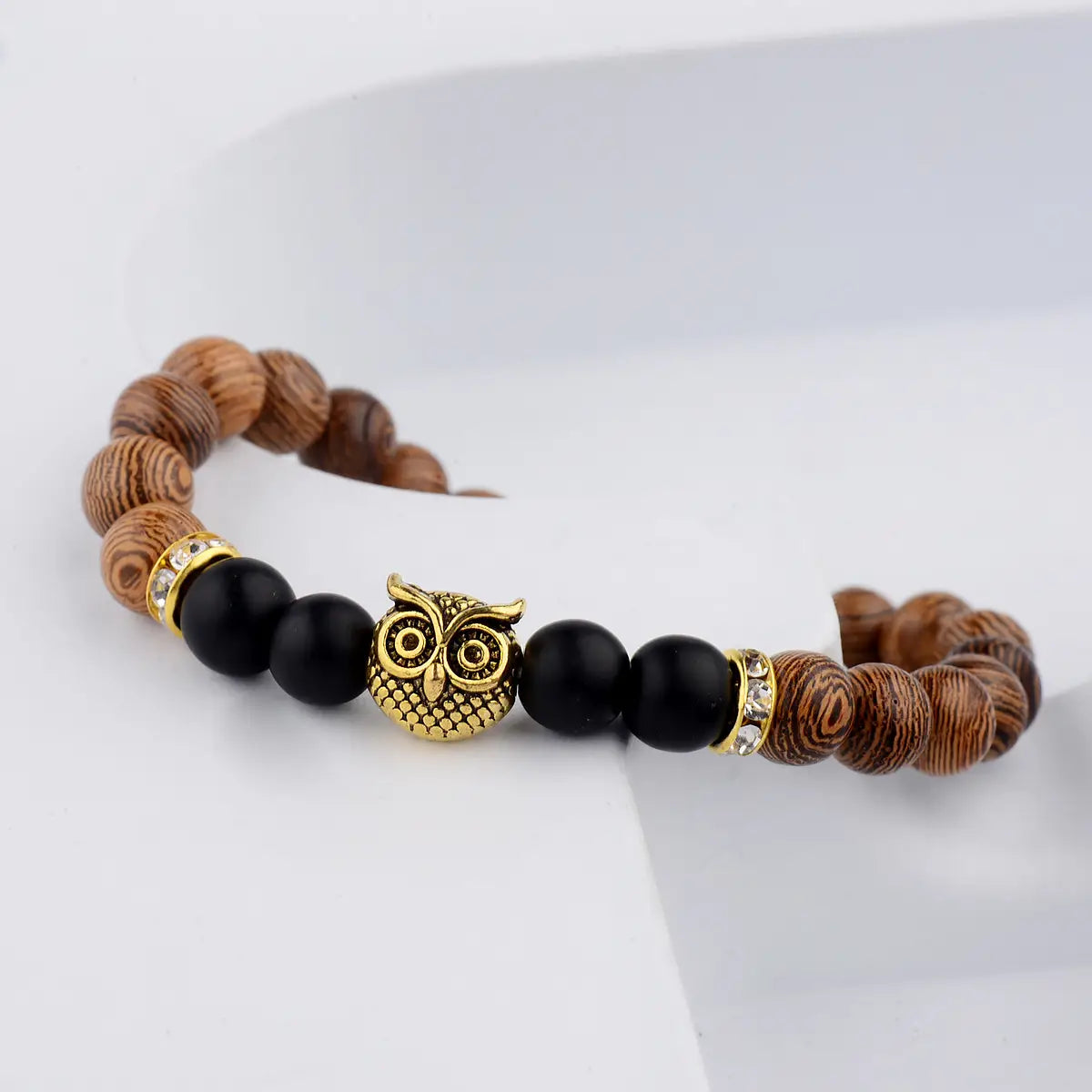 A crystal owl charm wood and onyx beaded bracelet featuring a gold owl charm with alternating natural wood and black beads with crystal accents.