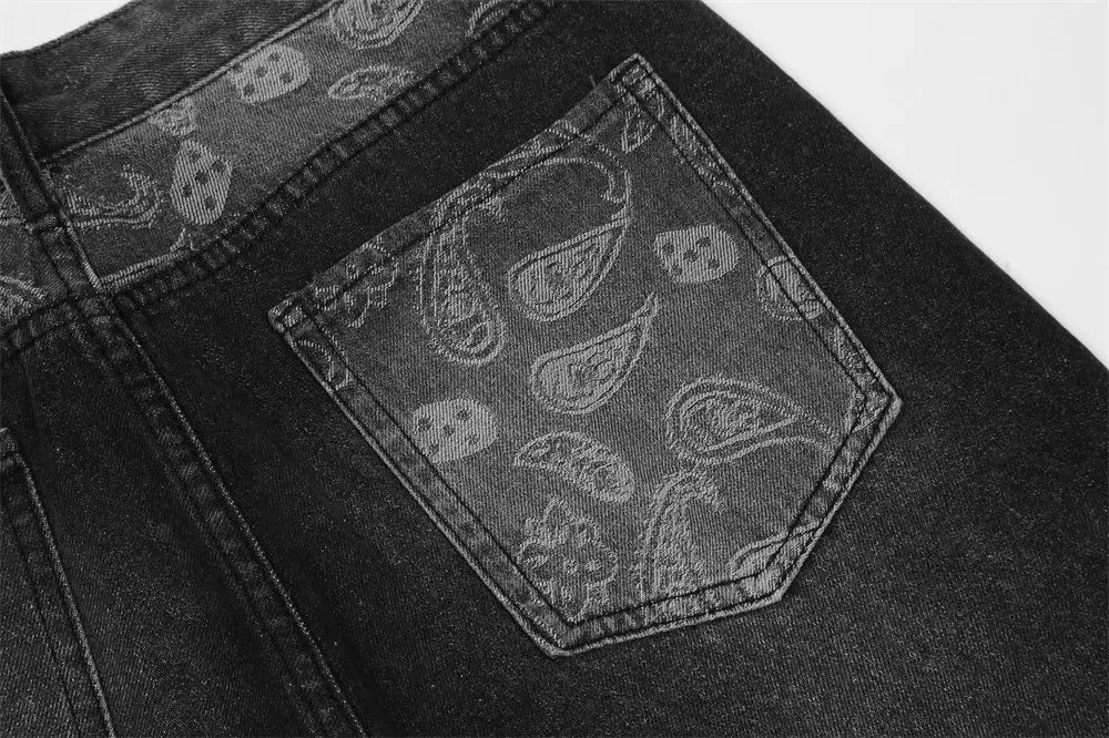 Men’s black denim distressed paisley patchwork flare jeans showing the back side with a back pocket featuring a subtle paisley and skull pattern.