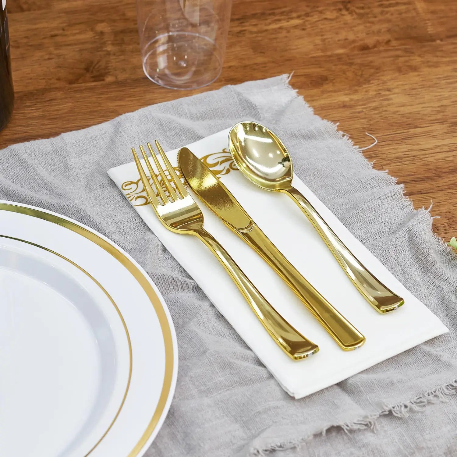 Gold-colored plastic cutlery set featuring a fork knife and spoon arranged neatly on a white napkin from a plastic tableware set with gold rim plates for 50 guests.