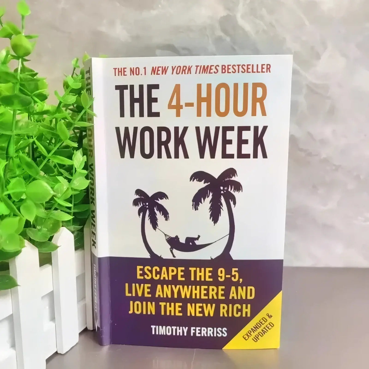 The 4-hour workweek timothy ferriss paperback book with white and purple cover featuring black palm trees and hammock illustration