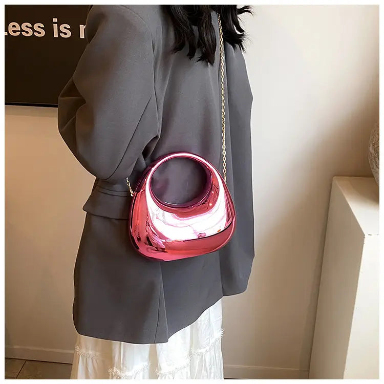 A glossy vibrant pink metallic acrylic clutch handbag featuring a unique circular handle and gold chain strap.