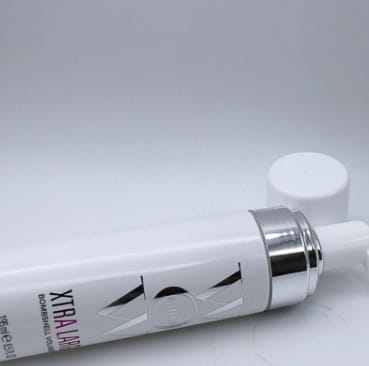 White cylindrical tube with silver metallic cap and black angular logo labeled xtra lift in bold pink text containing Color Wow Xtra Large Bombshell Volumizer hair mousse for volumizing hair.