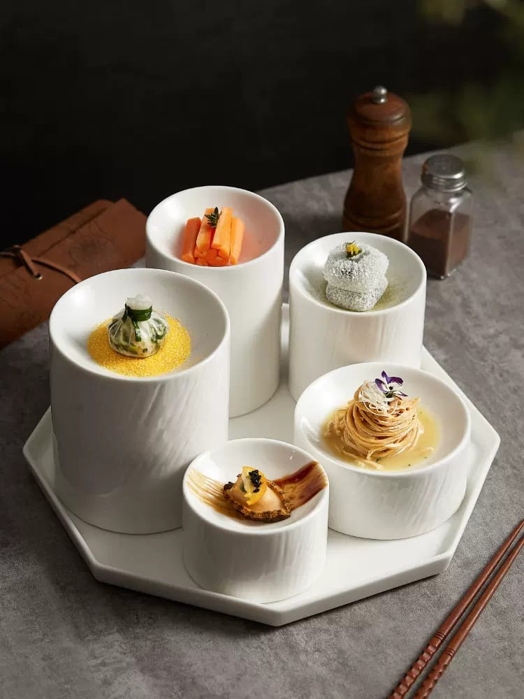 White ceramic appetizer bowls with a matte textured finish featuring ribbed sides arranged on a matching hexagonal serving tray.