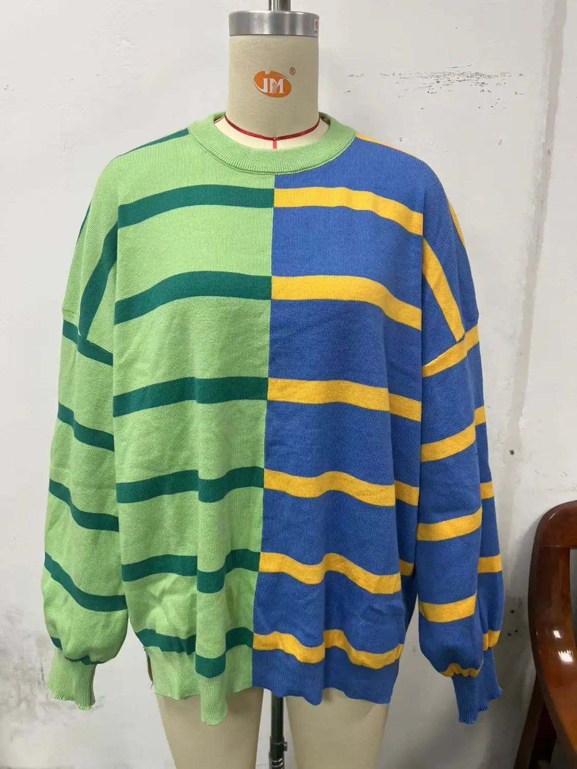 A vibrant women’s oversized knit sweater featuring a bold split design with lime green and dark teal stripes on one side and royal blue and mustard yellow stripes on the other.