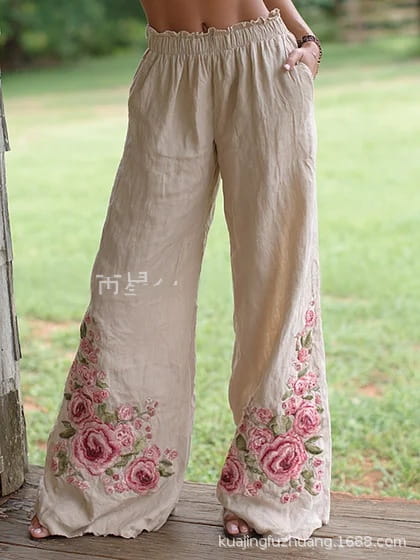 Pantalon décontracté ample à jambes larges en lin beige à imprimé numérique, avec une broderie de roses roses complexe le long des jambes inférieures.