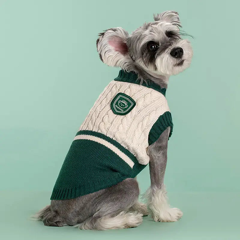 Ein gemütlicher cremefarbener und grüner Zopfmuster-Hundepullover mit weißen Streifen und kleinem besticktem Aufnäher auf der Brust, entworfen als warme Schuluniform-Tierbekleidung.