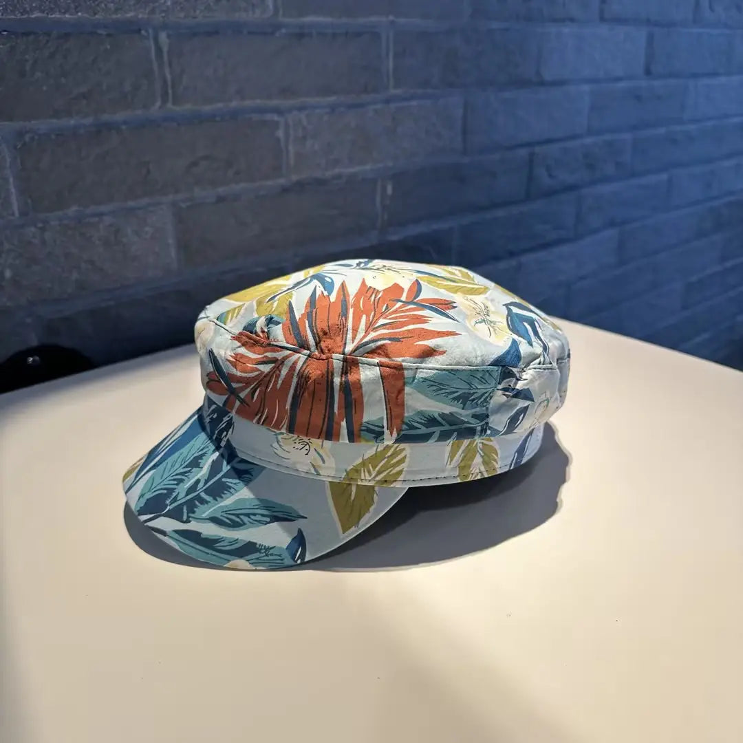 Gorra tipo bucket hat floral vibrante, estilo coreano, impresa, con parte superior plana y ala ancha, con hojas audaces en naranja, teal, amarillo y verde sobre un fondo azul claro.