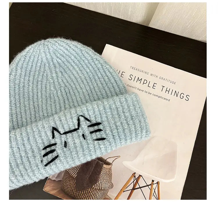 Light blue knitted beanie hat featuring a black embroidered cat face design.