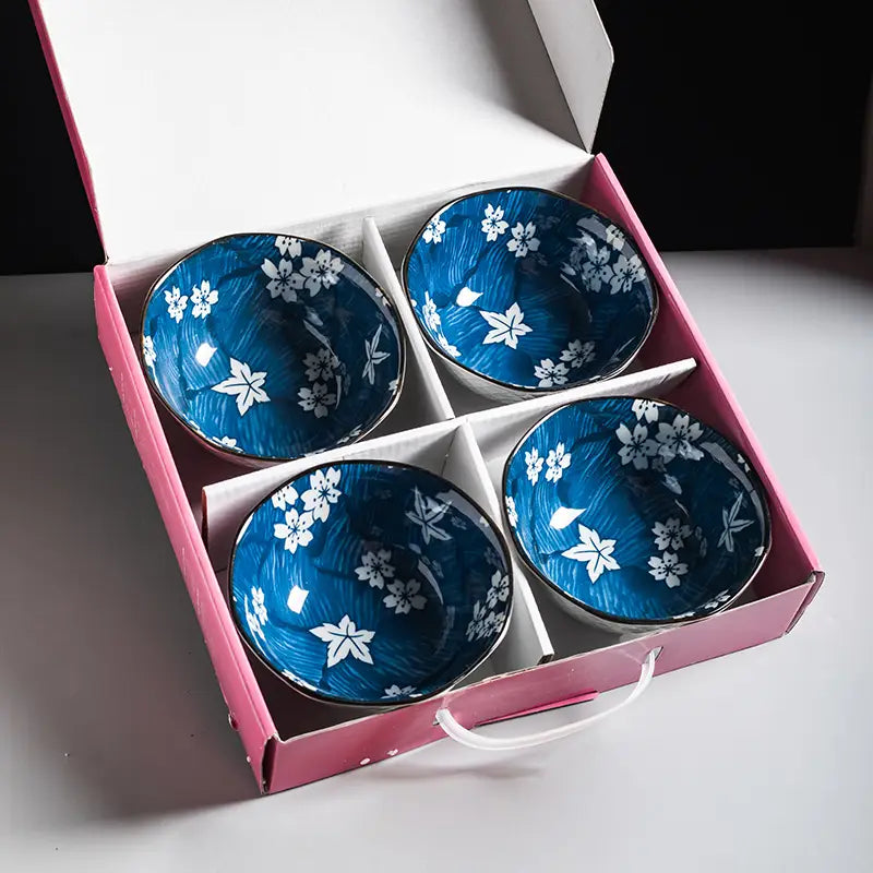 Set of four blue ceramic bowls with white floral patterns and gold rims made of porcelain neatly arranged in a pink gift box.