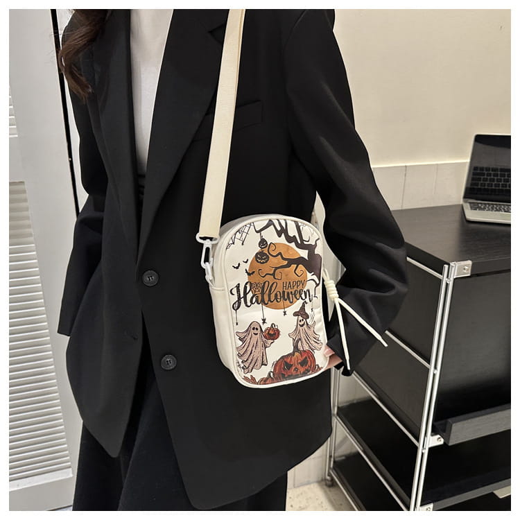 White embroidered Halloween floral and pumpkin crossbody bag featuring black and orange illustrations of ghosts pumpkins and a witch’s hat.
