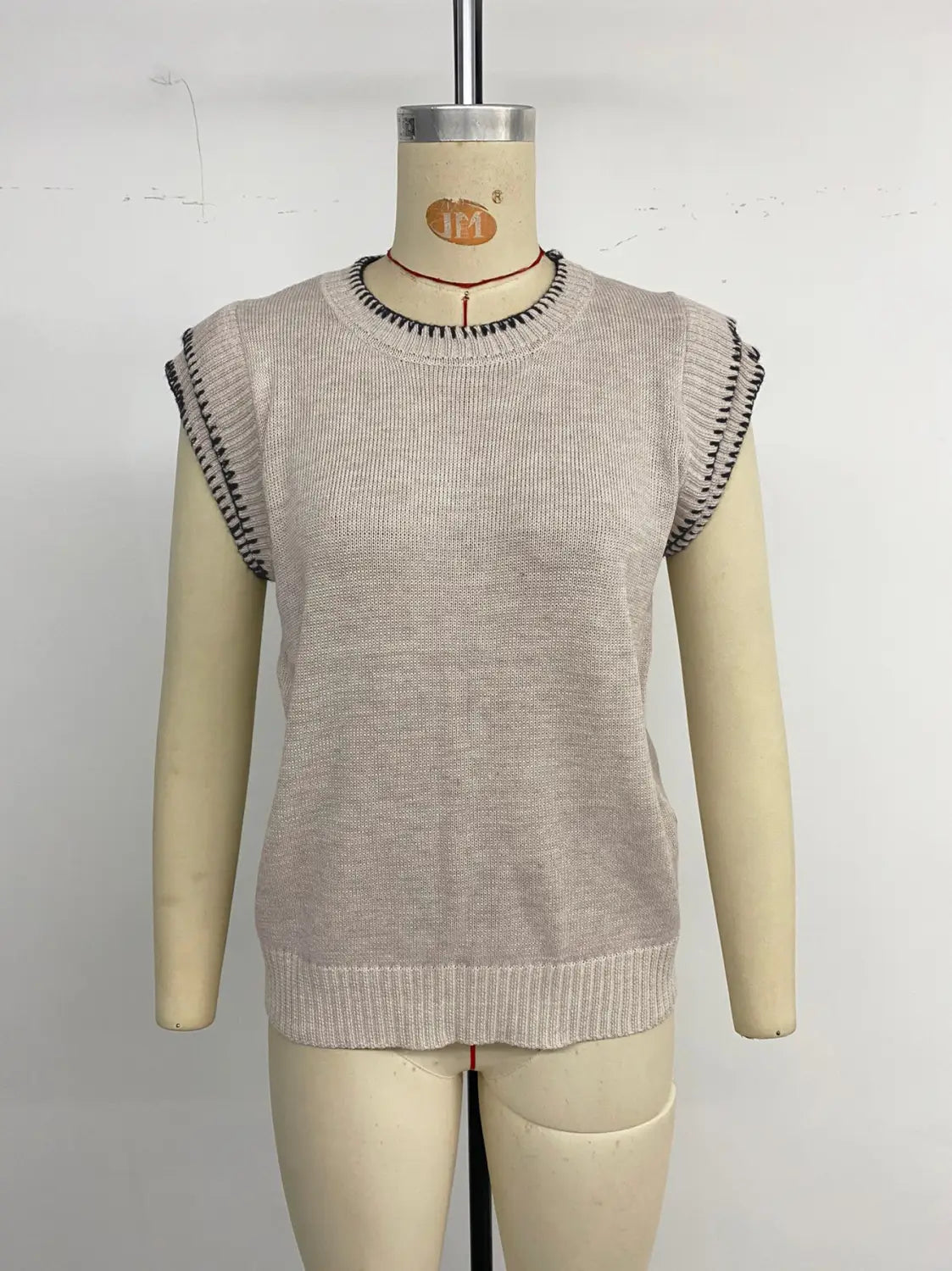 Haut sans manches en maille beige avec bords agrémentés d’un passepoil noir, présenté sur un mannequin avec un design à passepoil contrastant.