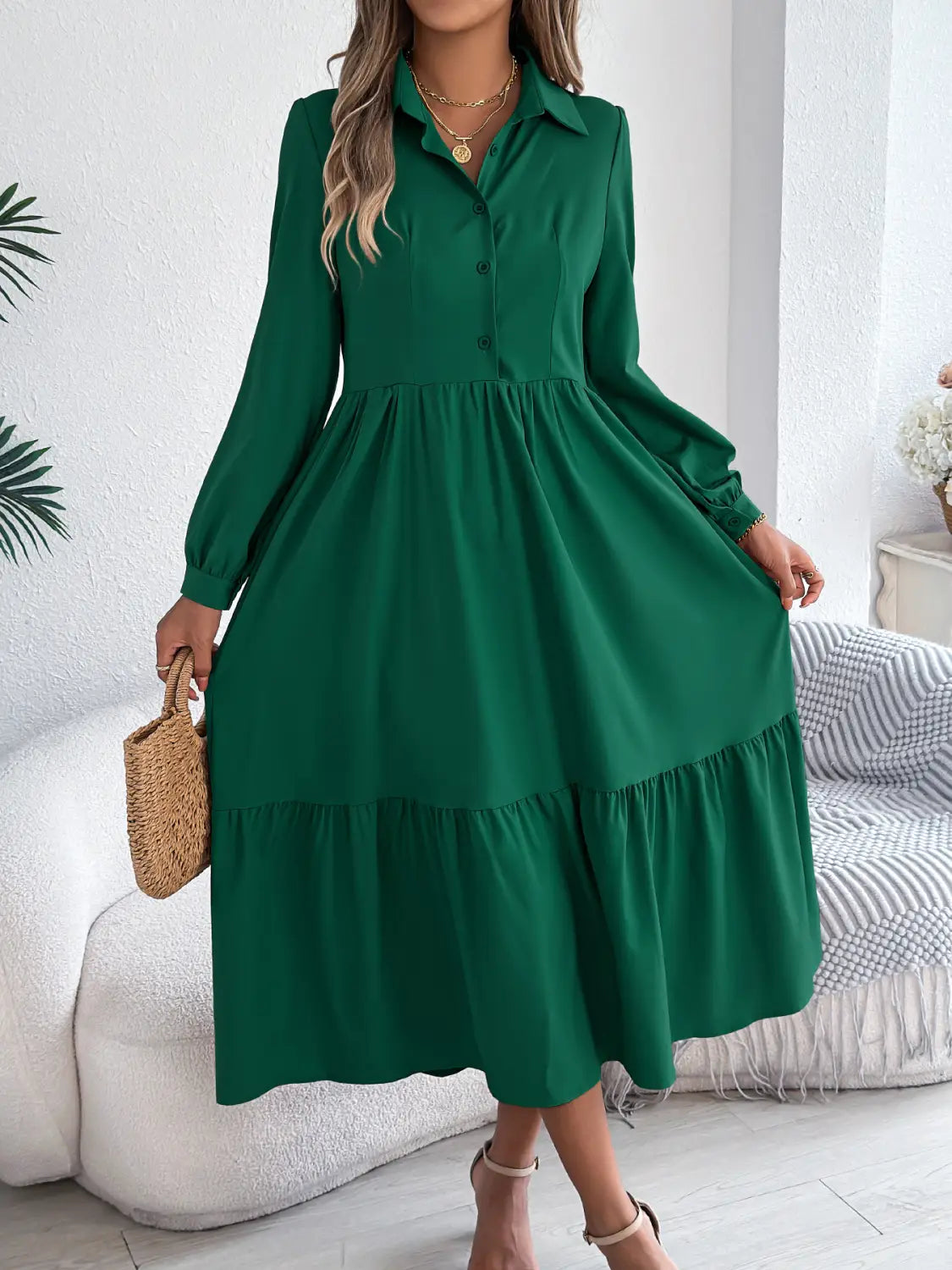 A woman wears a long sleeve emerald green tiered button down midi dress with a button front collar and ruffled hem.