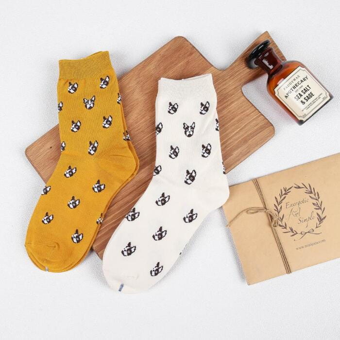 A pair of cute dog cartoon cotton crew socks in warm mustard yellow and soft off-white featuring a playful pattern of black french bulldog faces.