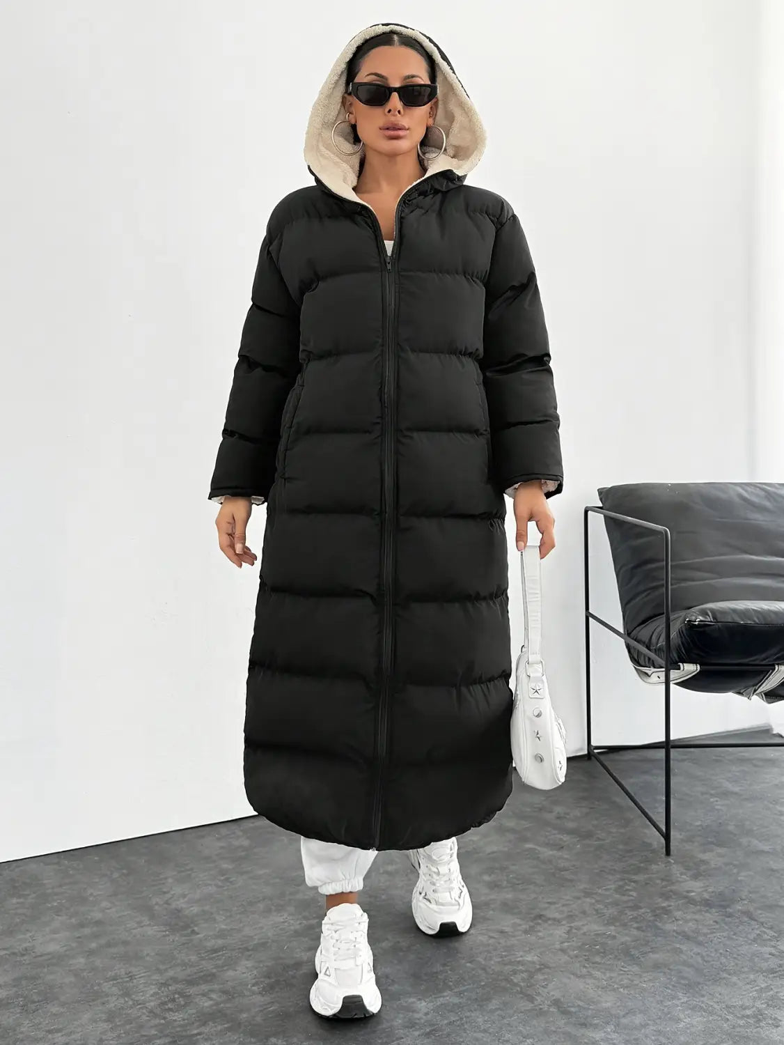 Black hooded quilted long puffer coat featuring a black exterior with a plush beige-lined hood and a quilted design.