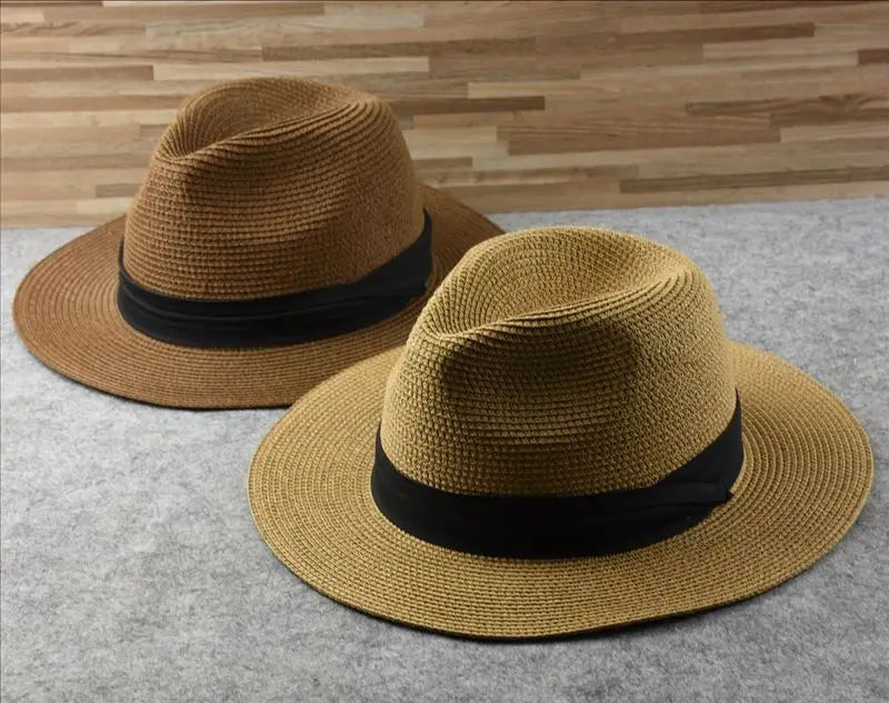 Two tan straw fedora hats with black ribbon bands designed for foldable sun protection for men.