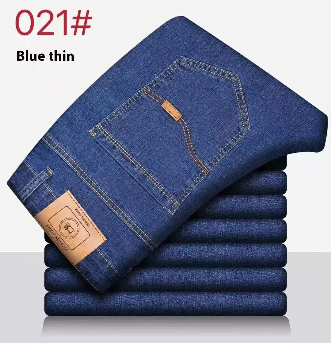 Jeans pour homme en denim bleu élastique à taille haute, avec écusson de marque en cuir camel et coutures contrastantes, conçus pour un port d’affaires décontracté.