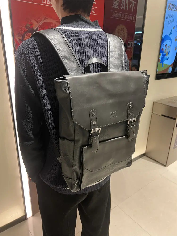 Dark gray leather vintage college backpack with large capacity travel bag flap closure secured by two metal buckles and small embossed logo on the front.