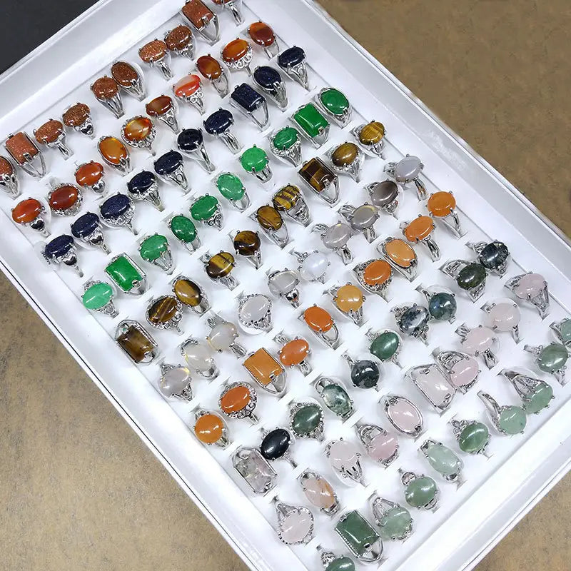 a collection of natural gemstone silver tone statement rings featuring colorful oval and rectangular stones in shades of orange green blue yellow pink white black and clear in silver toned metal settings