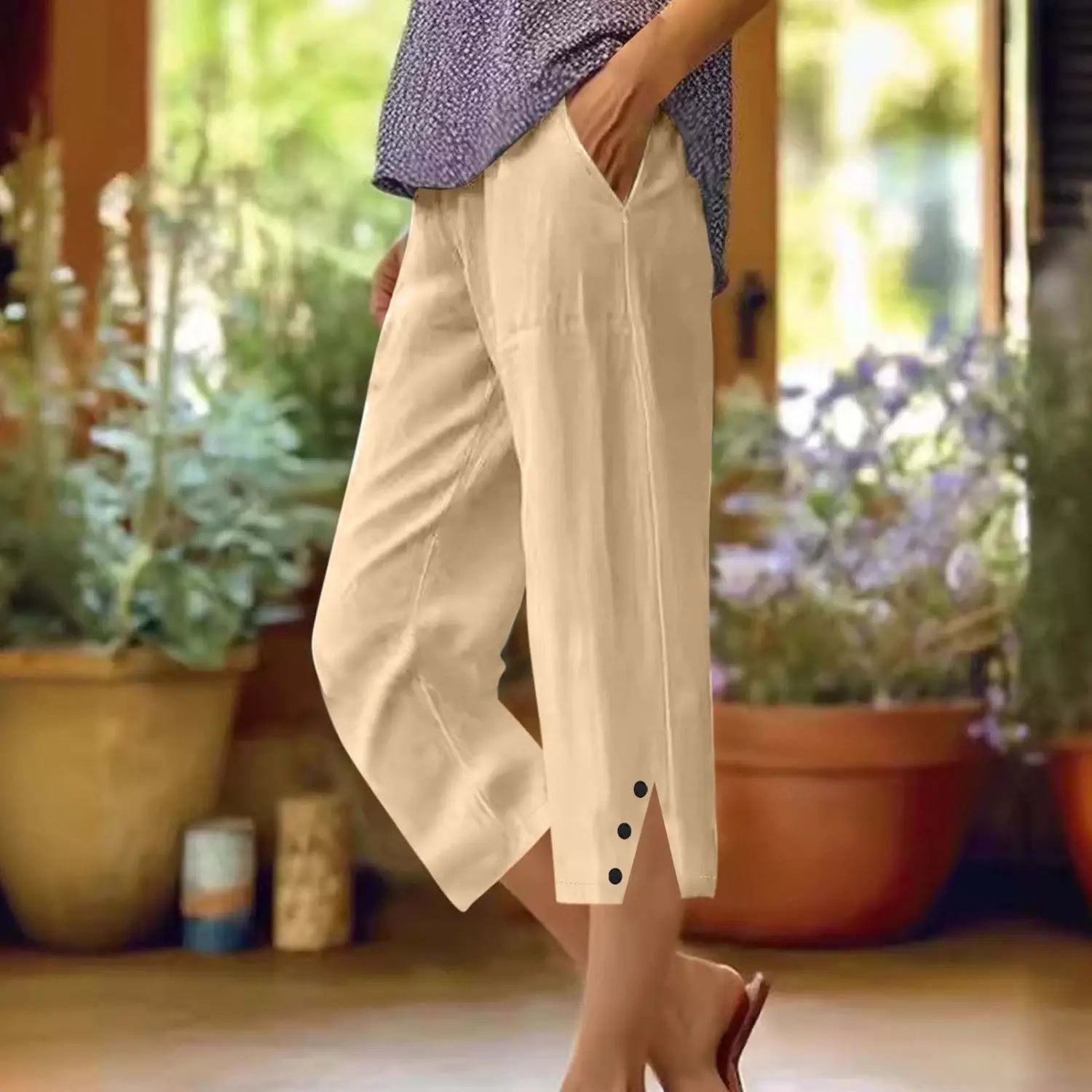 Pantalons capri en lin couleur crème ample en coton pour femmes avec poches, présentant une fente en bas et trois boutons noirs sur chaque jambe.