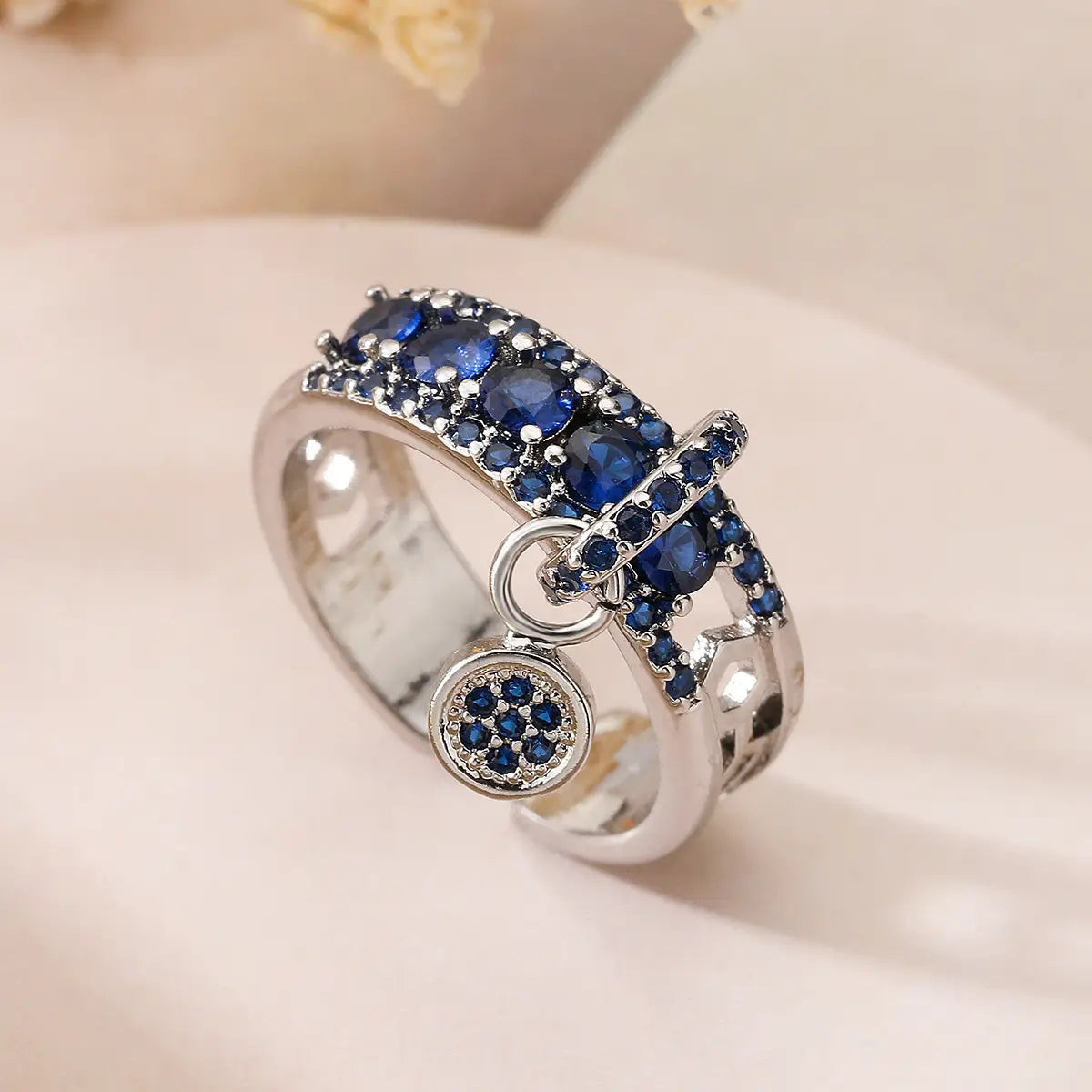 A silver adjustable open ring featuring deep blue zircon gemstones on the band and a circular charm adorned with smaller blue stones.