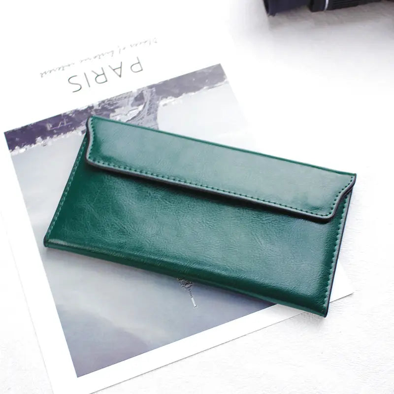 Deep green leather long wallet slim minimalist cowhide clutch with envelope-style flap closure and visible stitching along the edges.