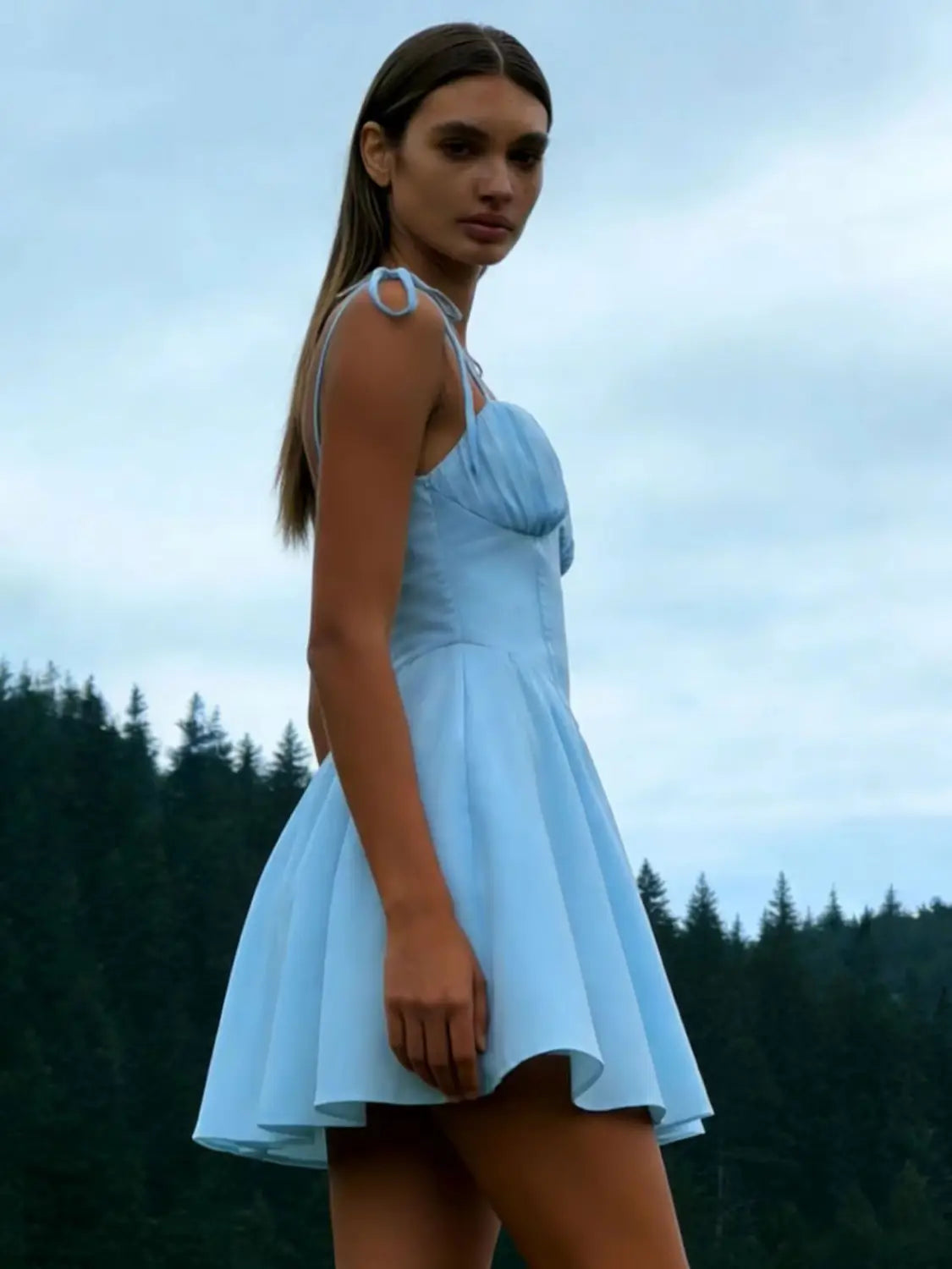 A sky blue ruched corset mini dress with a gathered bodice and thin shoulder tie straps featuring circular cutouts.