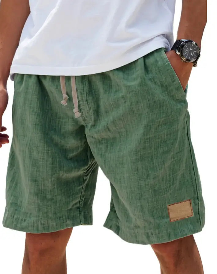 Men linen holiday shorts in olive green textured cotton with beige drawstrings and a tan patch on the side seam designed for a retro breathable loose fit.