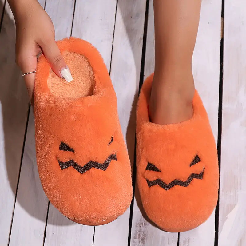 Orange plush Halloween pumpkin indoor slip-on slippers with black embroidered facial features.