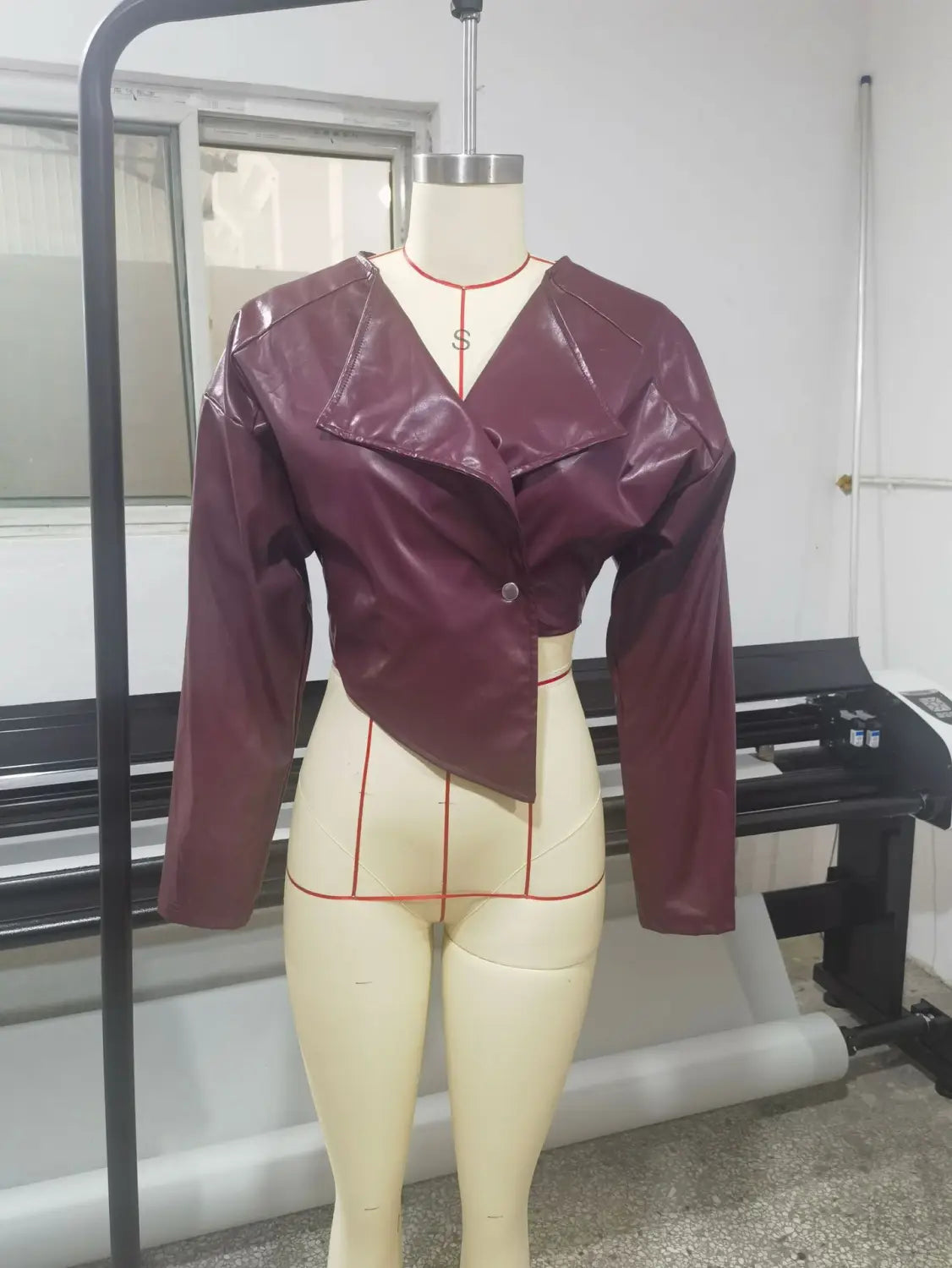 A glossy maroon faux leather cropped blazer for women featuring an asymmetrical front and single button closure.