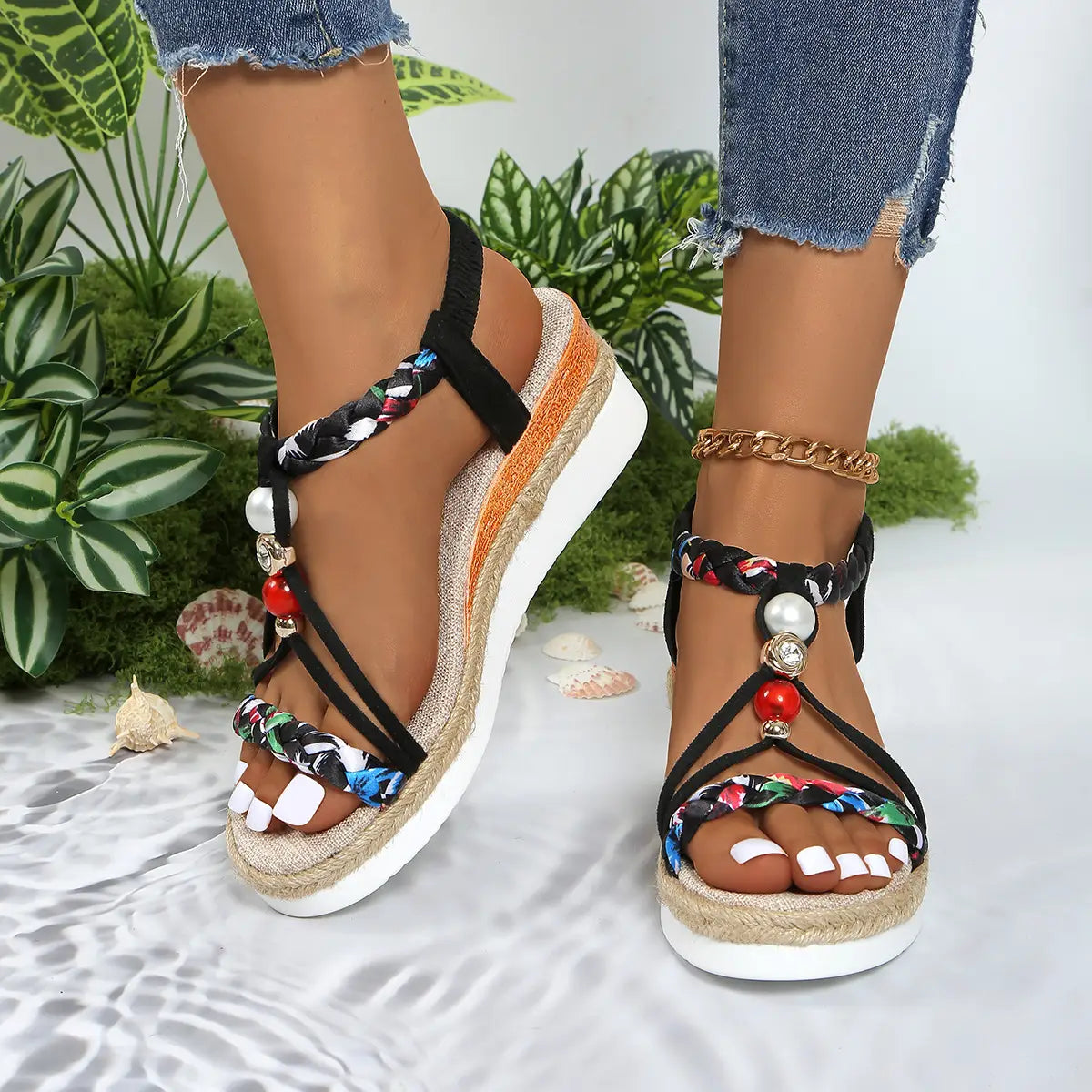 Sandalias tipo cuña para mujer con bailarinas espadrille tejidas, con correas trenzadas negras y multicolor, cuentas decorativas tipo perla y acentos rojos en una suela de plataforma blanca.