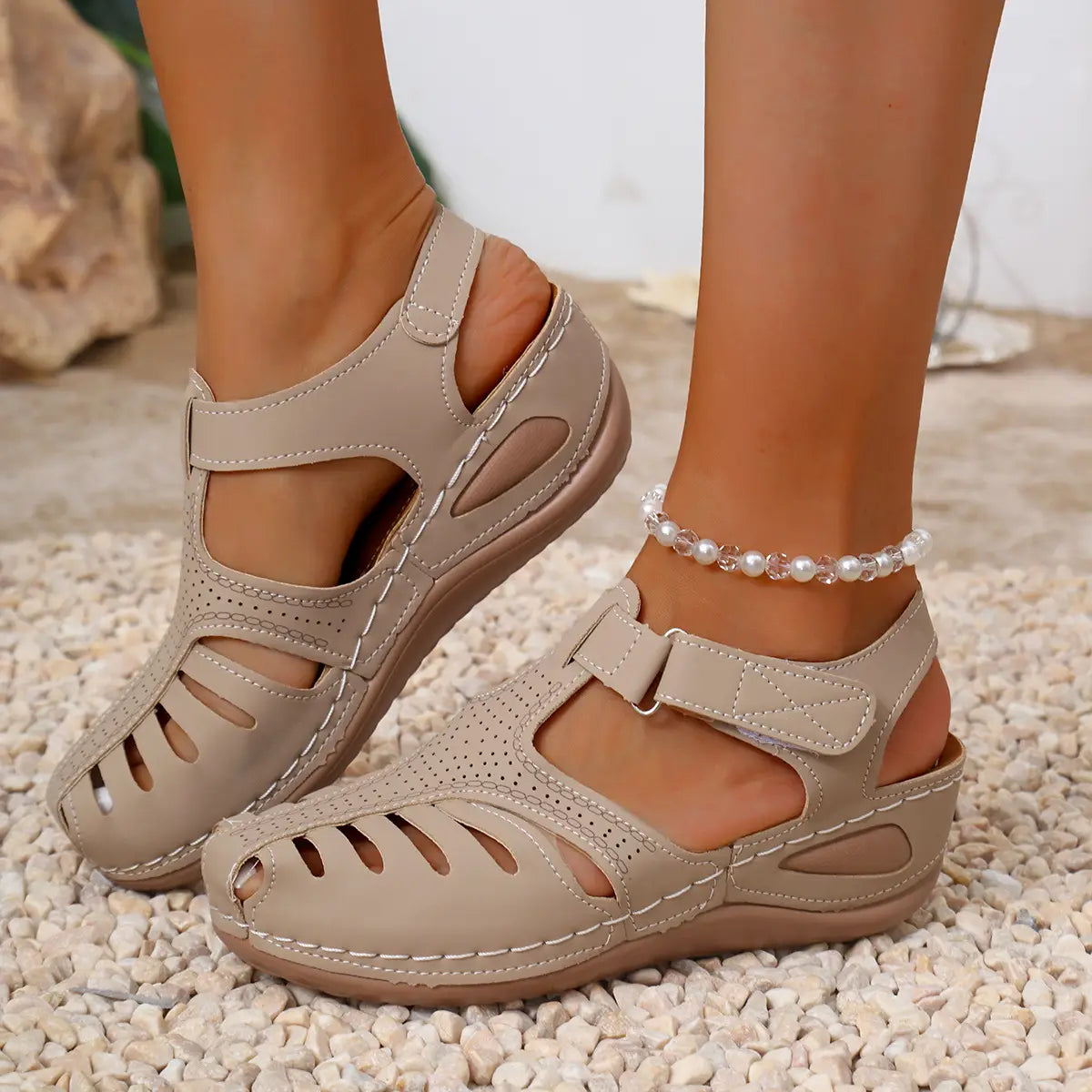 Sandales compensées en cuir beige pour femmes, avec dessus en cuir perforé et fermetures à bride réglable, conçues comme des chaussures d’été au style romain.
