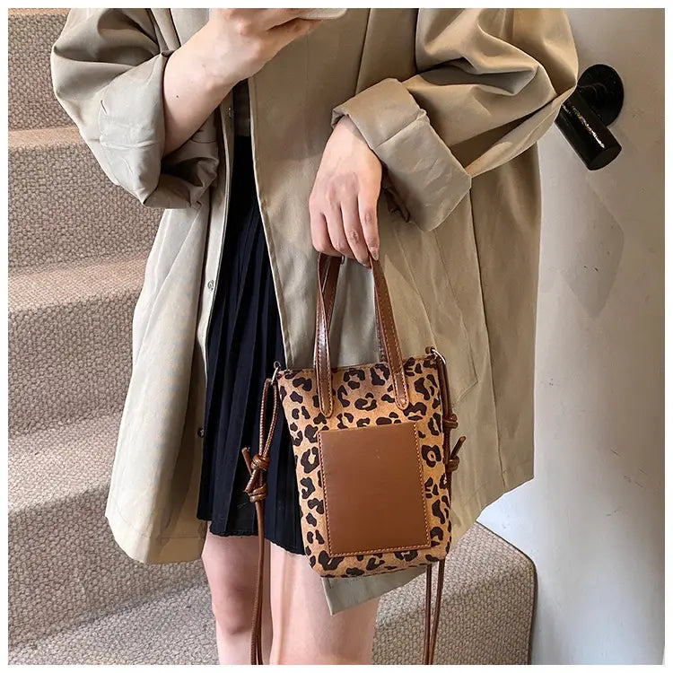 retro leopard print suede mini bucket crossbody bag with leopard print pattern brown leather handles and a solid tan rectangular panel