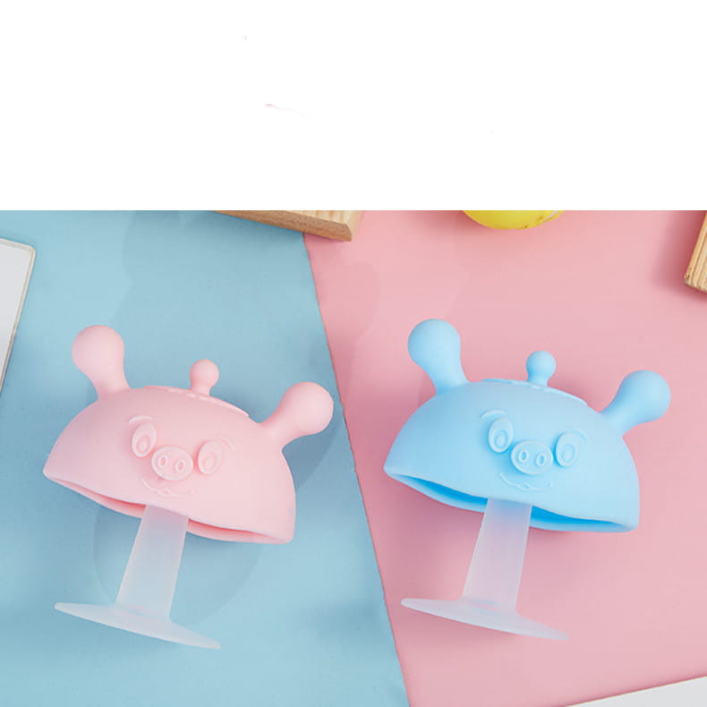 silicone baby teether and pig shape toothbrush holder in pink and blue made of silicone shaped like pigs with antennae.