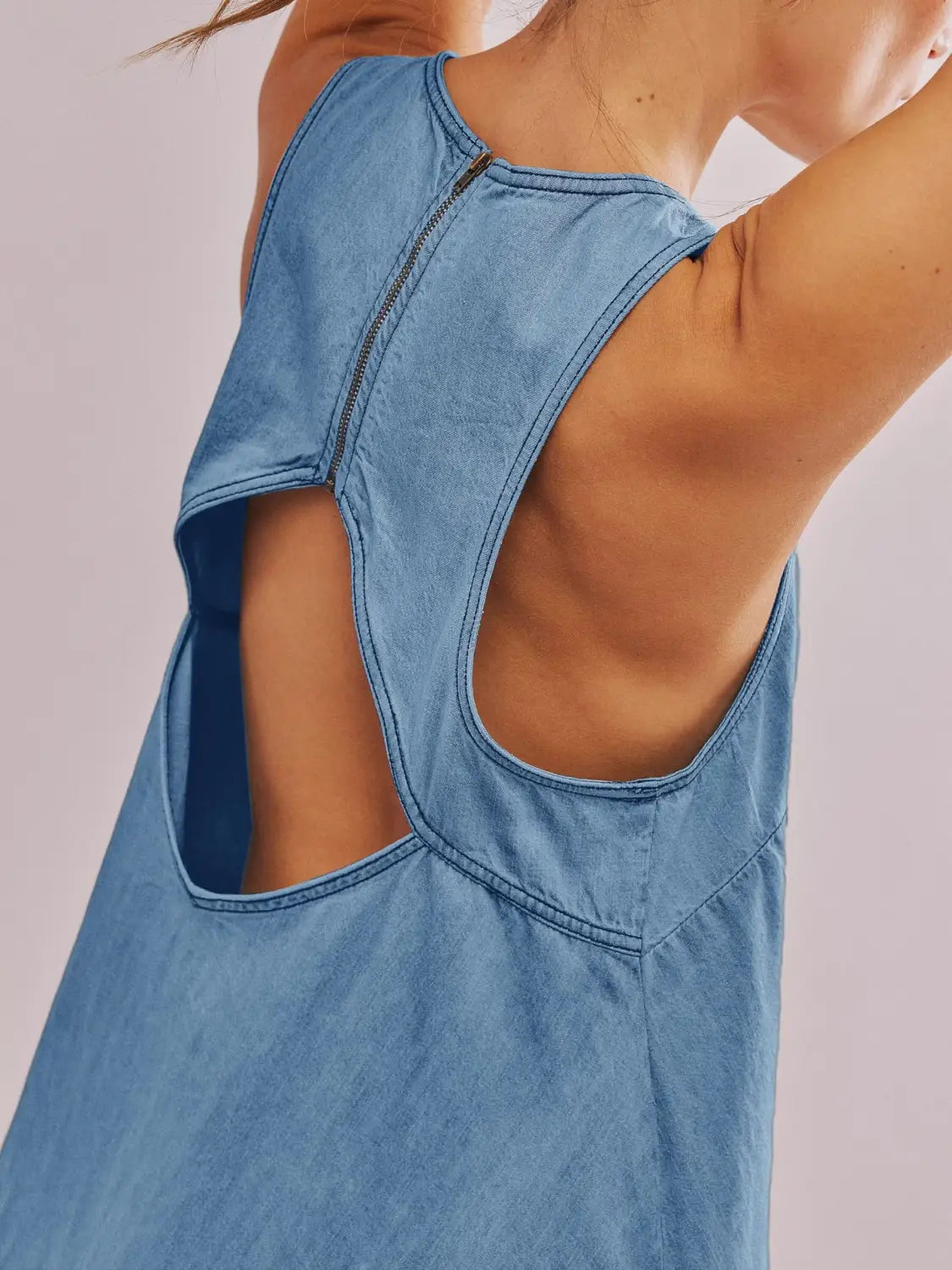Die Rückseite eines hellblauen Jeans-Minikleids zeigt ein hinten offenes Schleifen-Detail, einen rückseitigen Reißverschluss sowie Ausschnitt-Details.