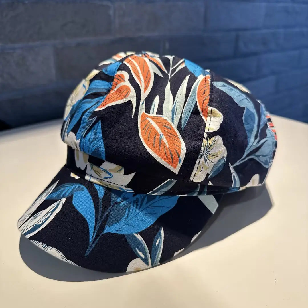 Floral newsboy cap for women featuring a vibrant floral pattern with bold orange blue and white leaves on dark navy fabric.