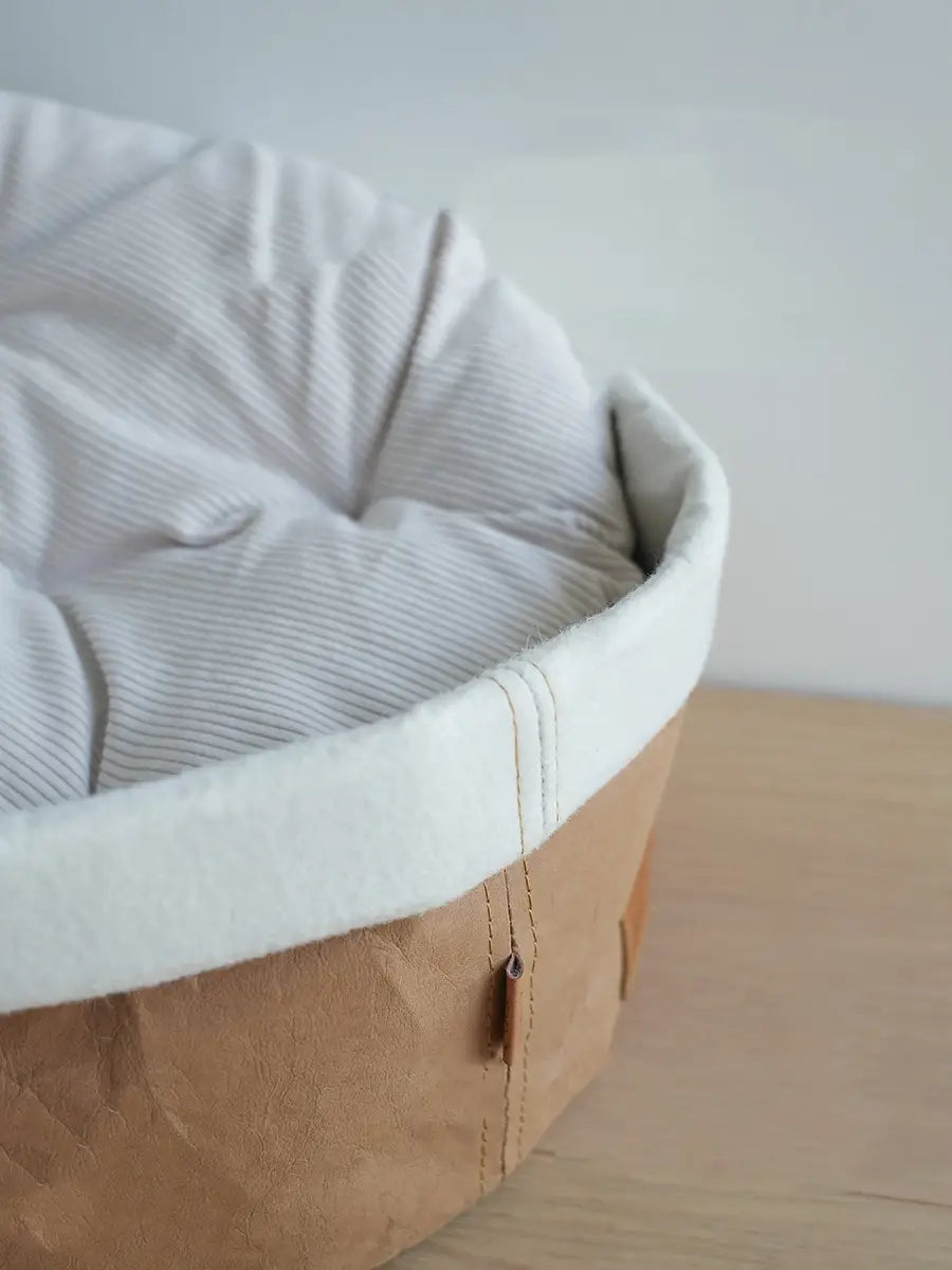 A cozy round pet bed with a soft white corduroy interior and a sturdy brown kraft paper exterior designed as a washable dog and cat nest.