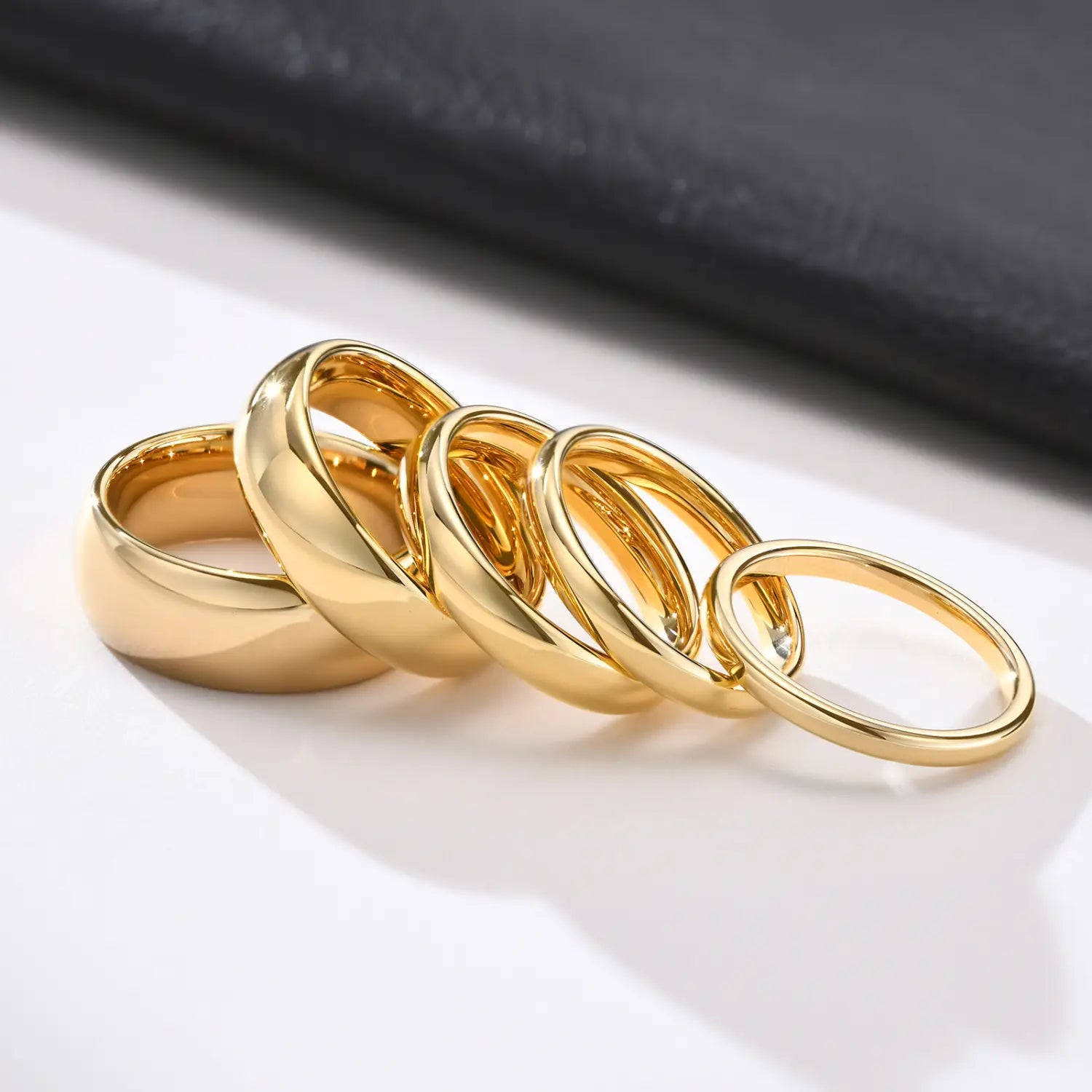 A set of five polished gold tungsten steel couple wedding bands with smooth surfaces and varying widths.