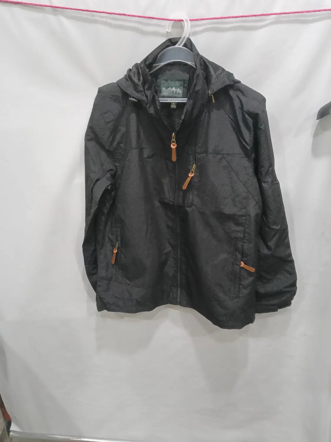 Chaqueta de senderismo con capucha impermeable color negro, con tiradores de cremallera color camel, diseñada para actividades al aire libre.