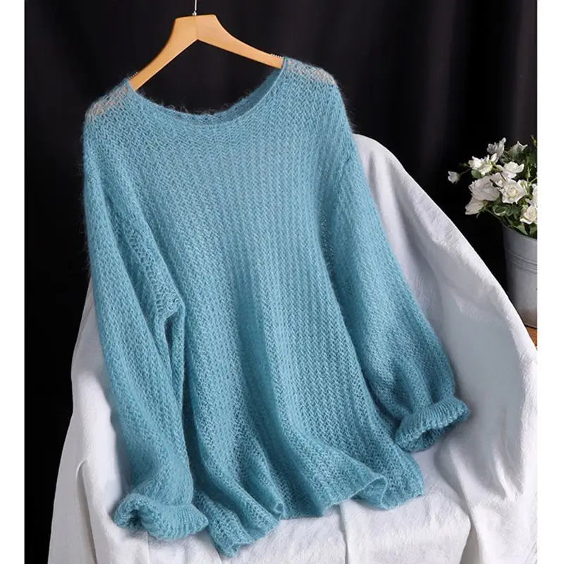 Ein weich leuchtend hellblauer Pullover in offener Strickoptik, als Blusenstil gestricktes Oberteil, mit lockerer Passform und gerippten Bündchen, hängt auf einem Holzkleiderbügel.