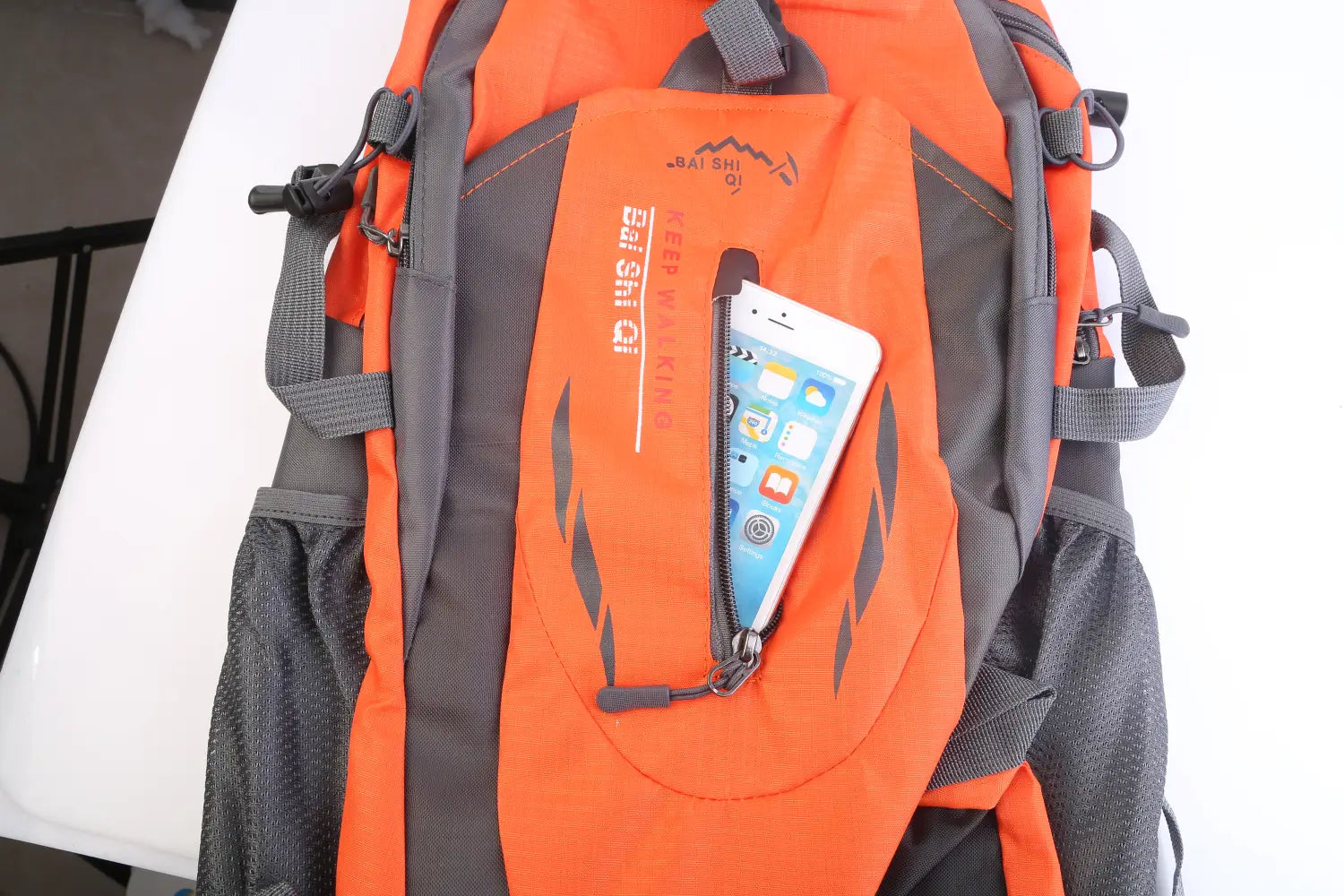 Orange and gray 36l lightweight waterproof hiking backpack with reflective stripes featuring a front zippered pocket holding a white smartphone.