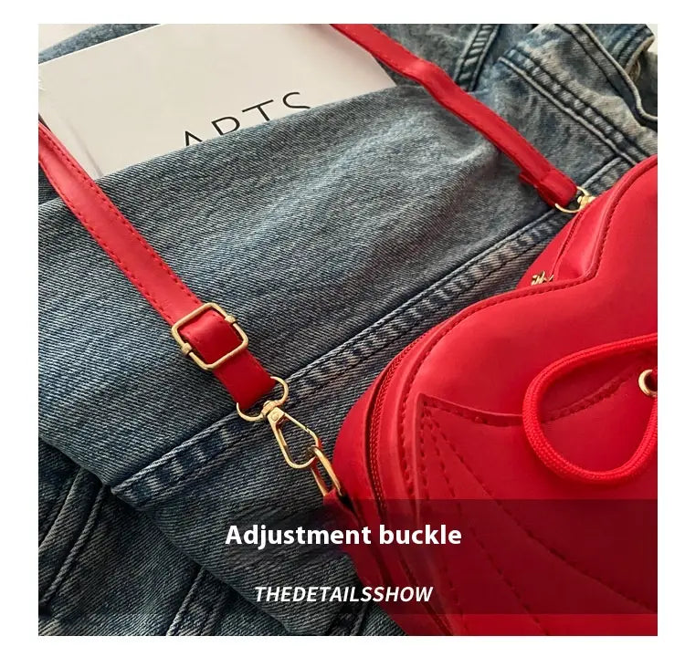 Vibrant red heart-shaped bat wing crossbody bag with matching strap gold-tone hardware and lace-up detail.