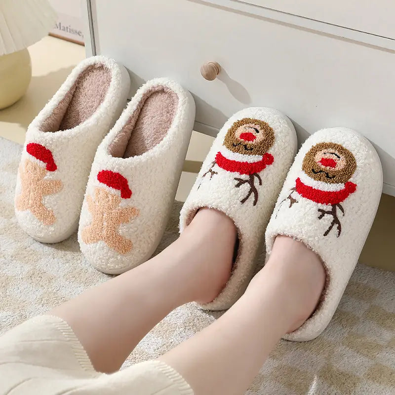 White plush slippers featuring festive embroidered reindeer and gingerbread man designs with red scarves and hats made from soft fleece material in a product titled Festive Embroidered Santa and Reindeer Winter Slippers.