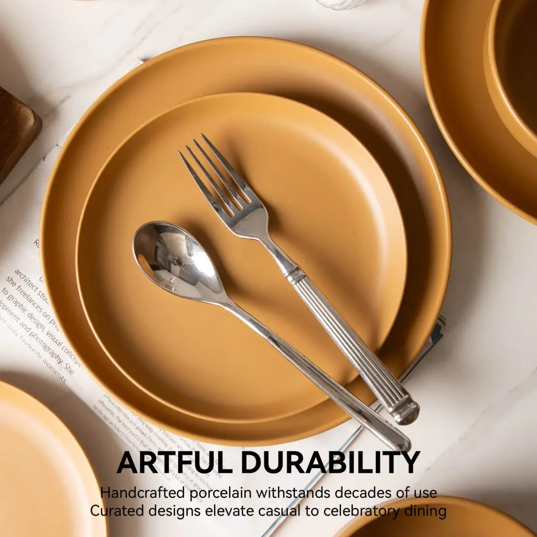 Set of handcrafted mustard-yellow stoneware dinnerware plates with matte glaze and matching silver-toned cutlery featuring ribbed handles for four people.