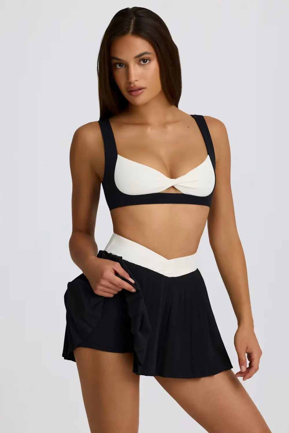 Schwarz-weißes zweiteiliges Swimwear-Set mit BH-Top mit Cut-out in der Mitte und dazu passende Shorts mit Rüschen-Detail an der Seite, ausgelegt für den plissierten Sportrock-Skort mit figurformender Fitnesswirkung.