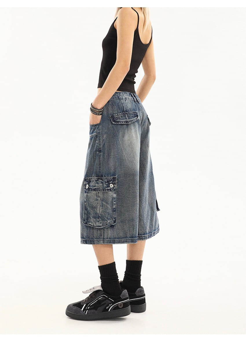 Falda cargo de mezclilla azul de largo a la mitad del muslo, con lavado azul desvaído y múltiples bolsillos, diseñada para un estilo urbano relajado.