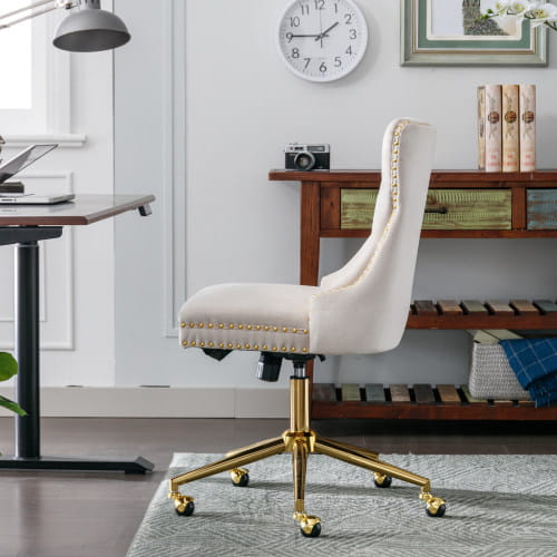 Silla de oficina tapizada en terciopelo color crema, con botones tipo capitoné, marco metálico de tono dorado y remate decorativo con tachuelas en color beige.