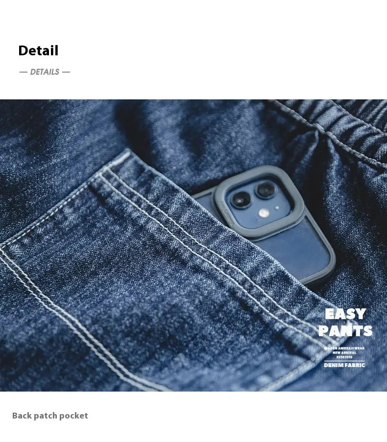 Un teléfono negro elegante con funda protectora gris descansa en el bolsillo trasero con parche de los pantalones vaqueros relajados y cónicos azul marino oscuro para hombre, fabricados en material de mezclilla.