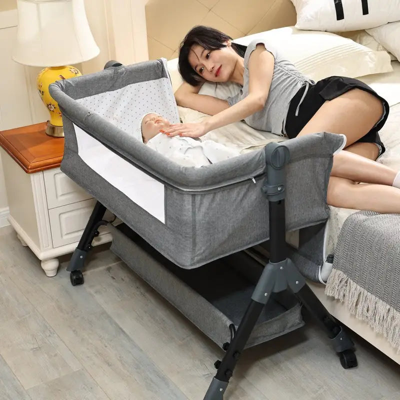Gray fabric portable folding baby crib with black metal frame and wheels featuring mosquito net and mattress is shown from the front.