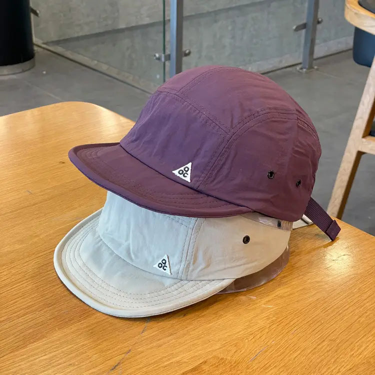 Purple and beige quick drying short brim five panel cap featuring a triangular logo on the front.